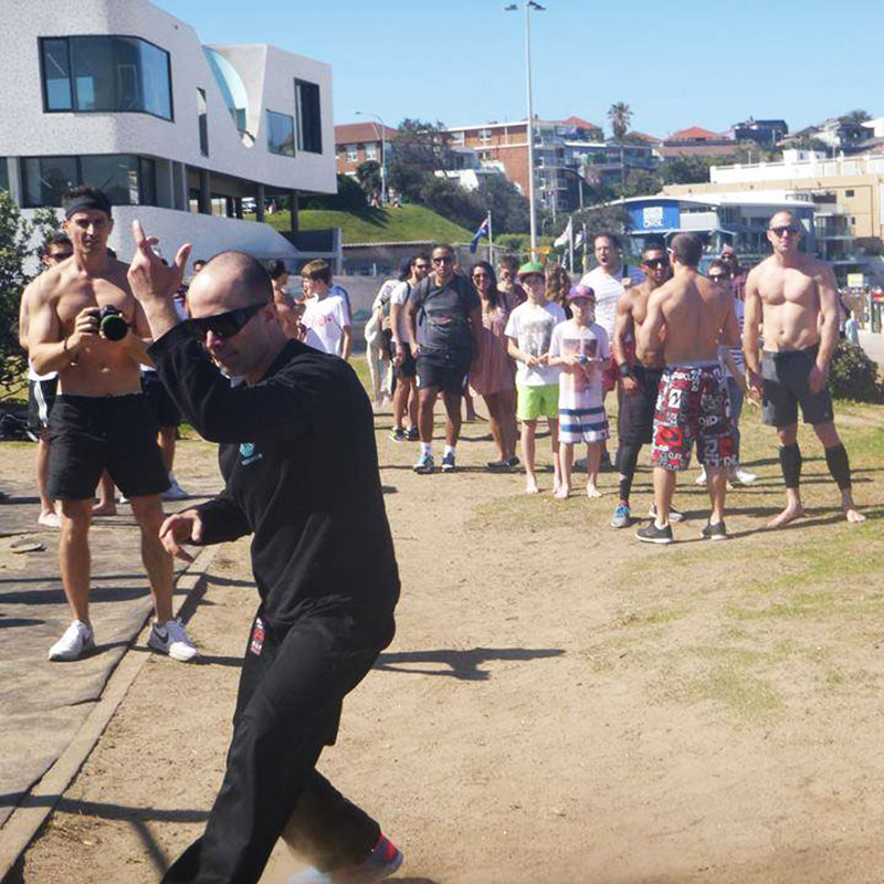 Live action demonstation of Xing Yi and Bagua 
        at Bondi Beach in front of a crowd of people. People watch as one man films.